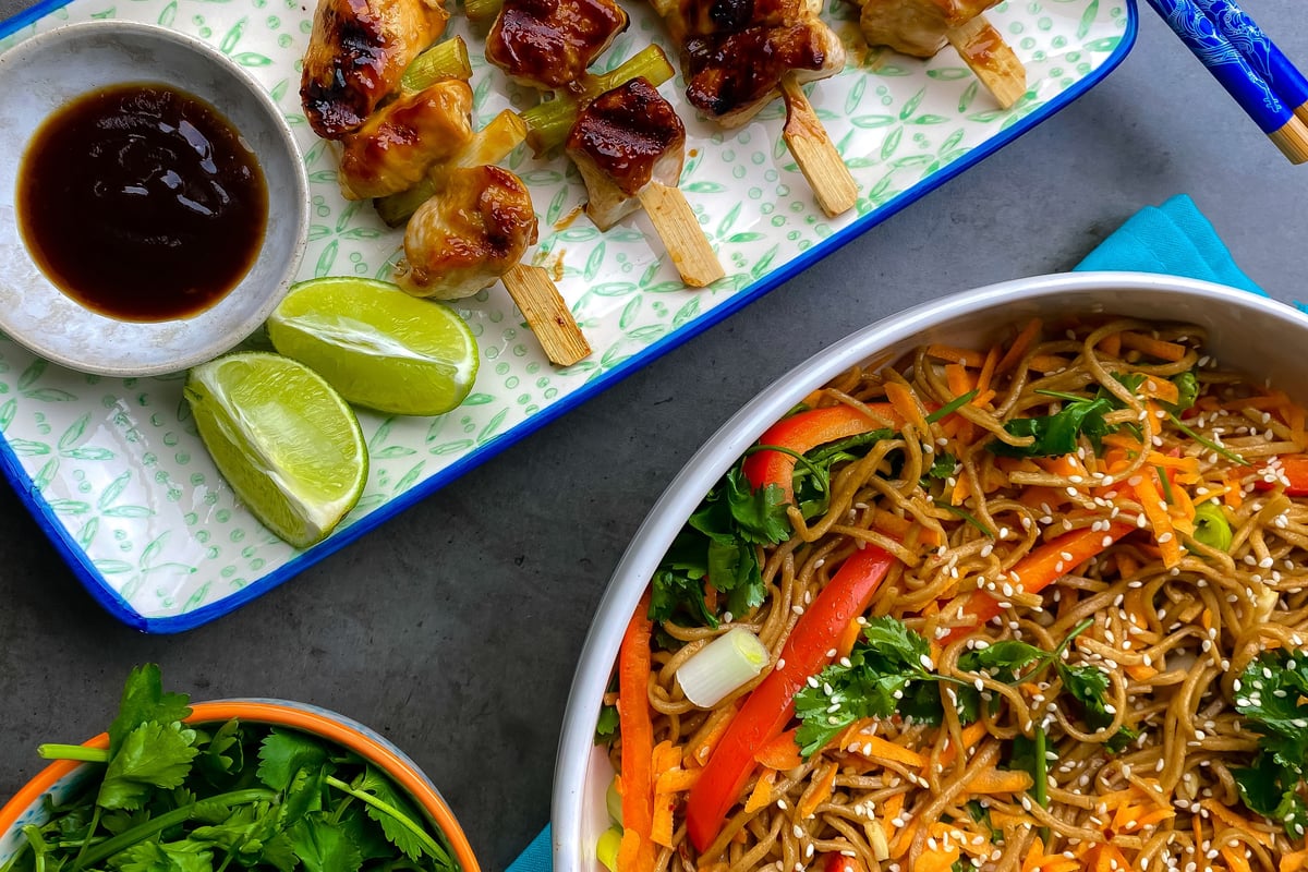 Chicken and vegetable skewers on wooden sticks with noodle salad and dipping sauce