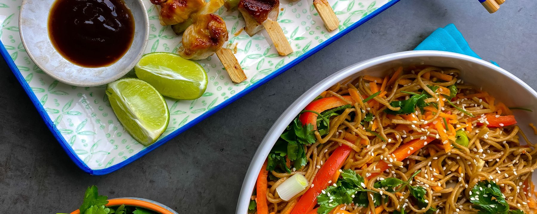 Chicken and vegetable skewers on wooden sticks with noodle salad and dipping sauce
