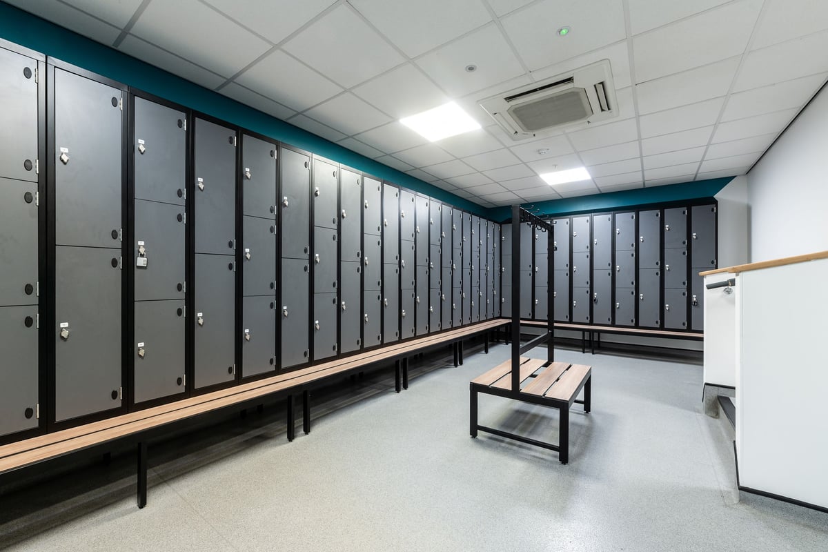 PureGym Ipswich Buttermarket: Rows of lockers, wooden benches in a teal room interior.