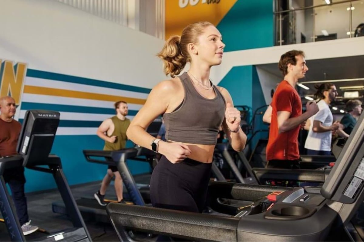 Personnes courant sur des tapis de course dans une salle aux murs rayés bleu et jaune