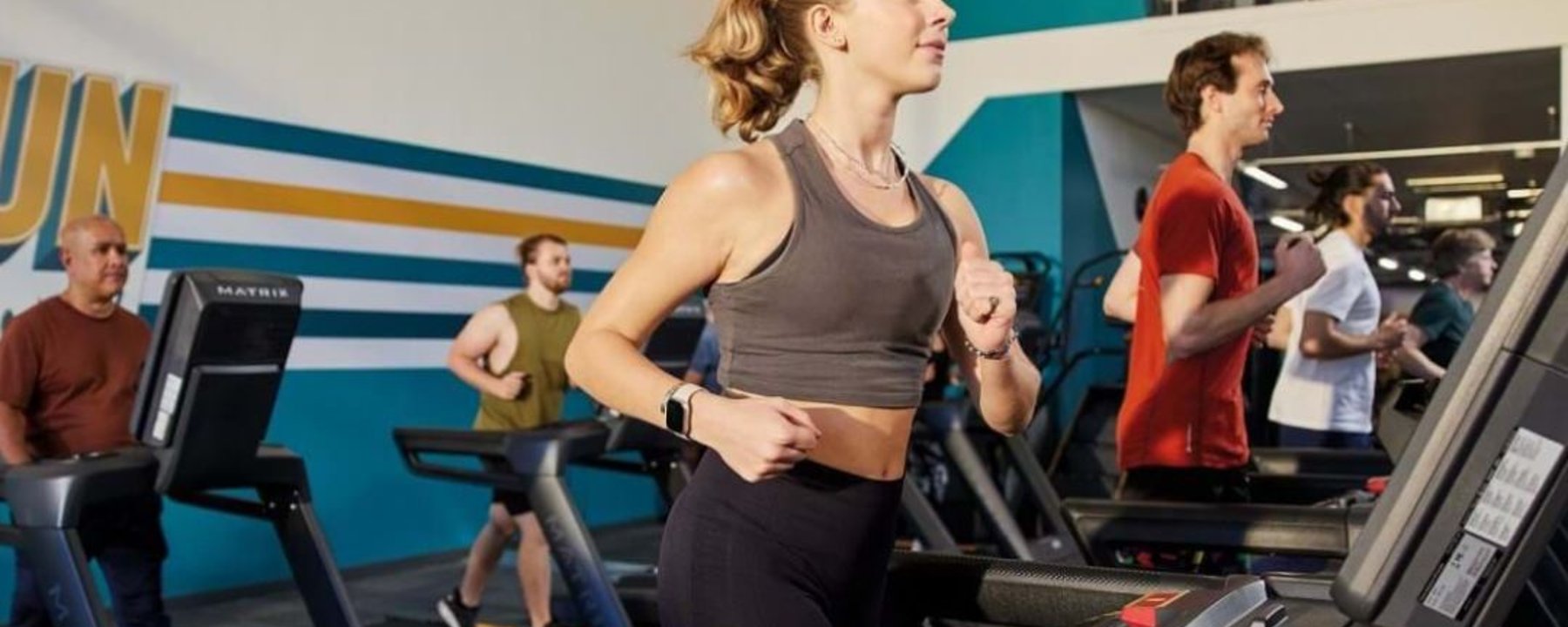 Personnes courant sur des tapis de course dans une salle aux murs rayés bleu et jaune