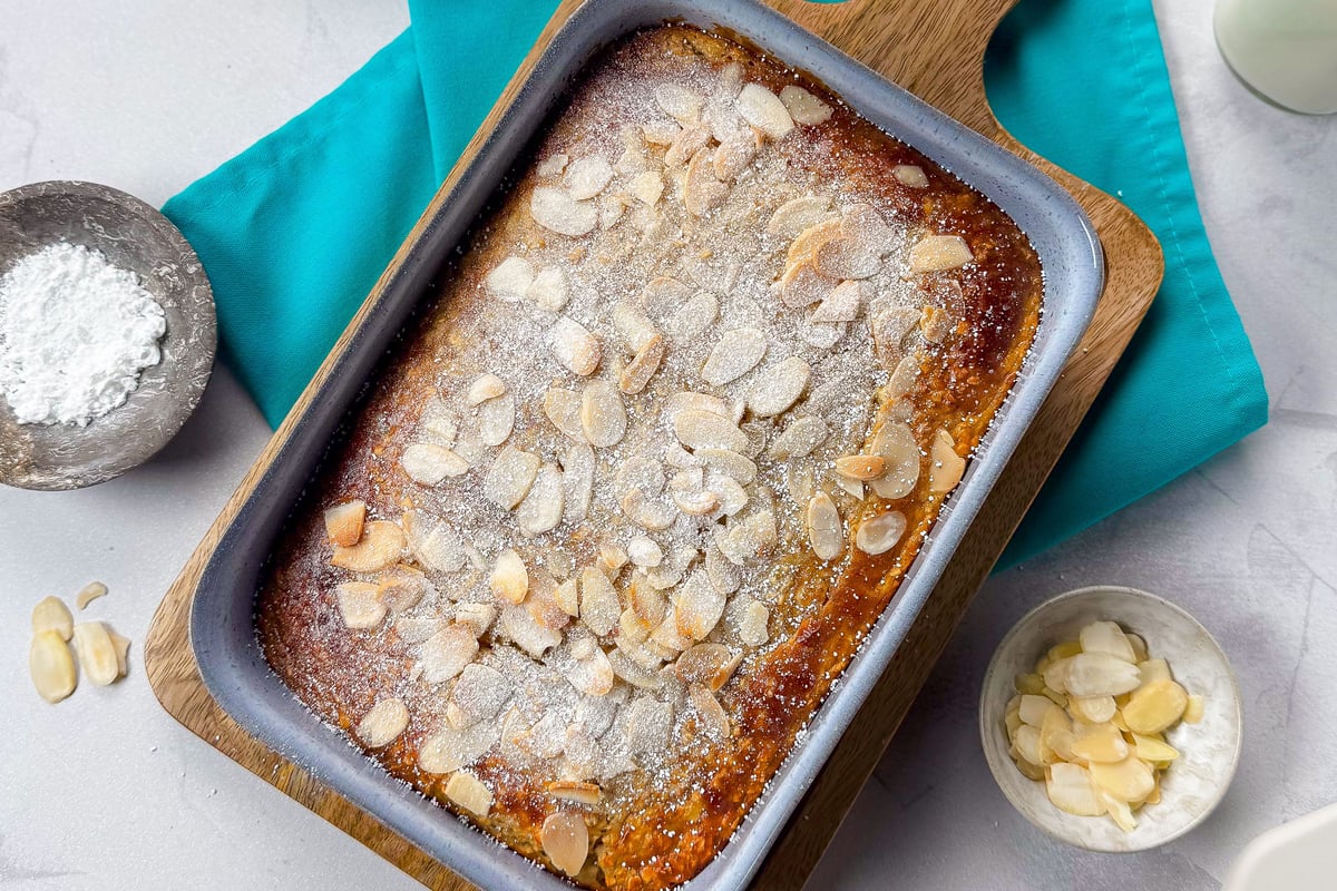 Baked oats topped with flaked almonds and icing sugar in a rectangular baking tin