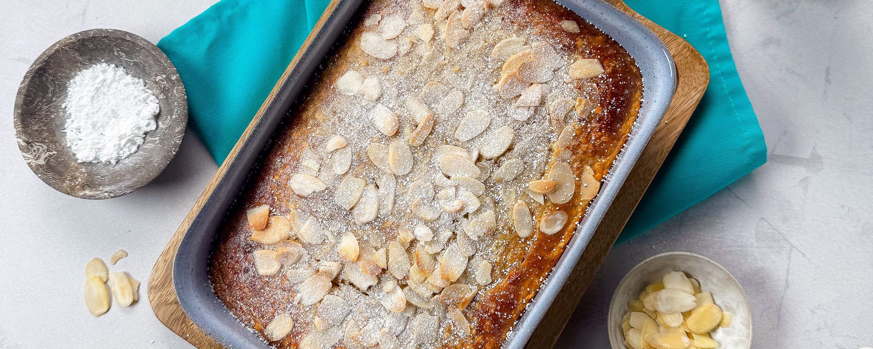 Baked oats topped with flaked almonds and icing sugar in a rectangular baking tin