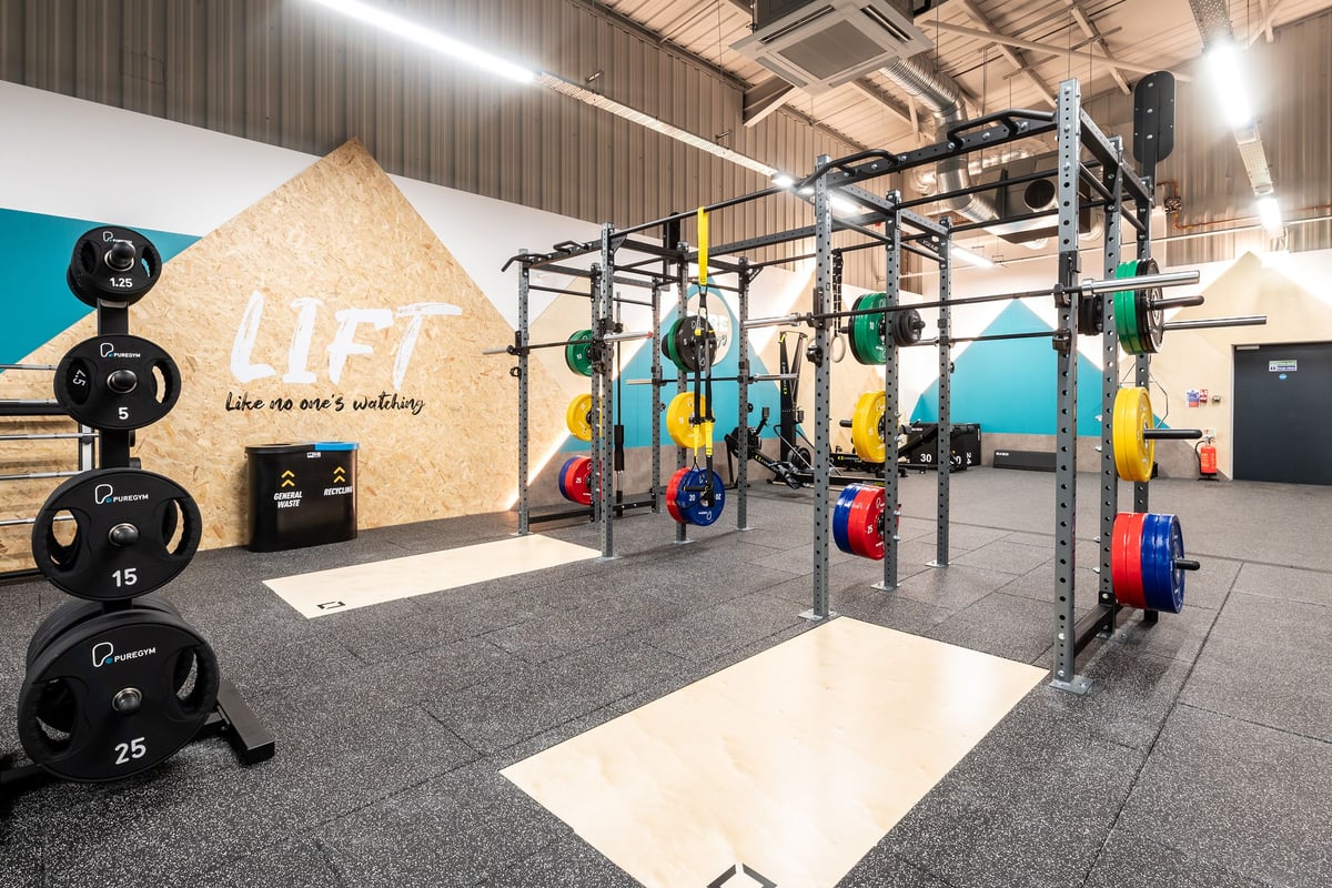 PureGym Alfreton: Rig with weight plates, kettlebells, rowers; rubberized flooring in an industrial-style gym.