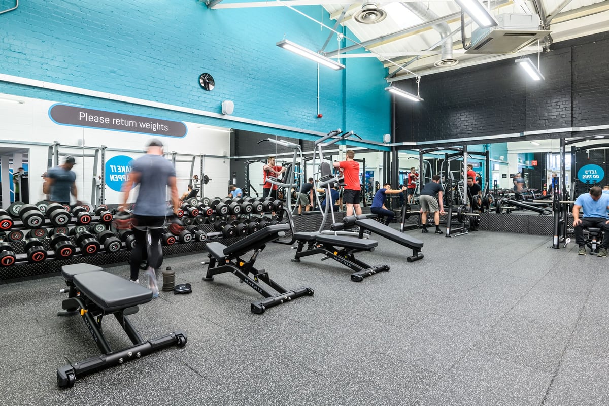 PureGym London Clapham: Weight racks, benches, dumbbells, and weight plates in a teal and grey gym interior.