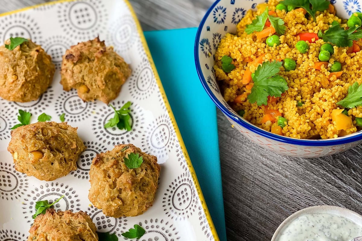 Baked falafel balls on a patterned tray, bowl of couscous with vegetables, and sauce bowl.