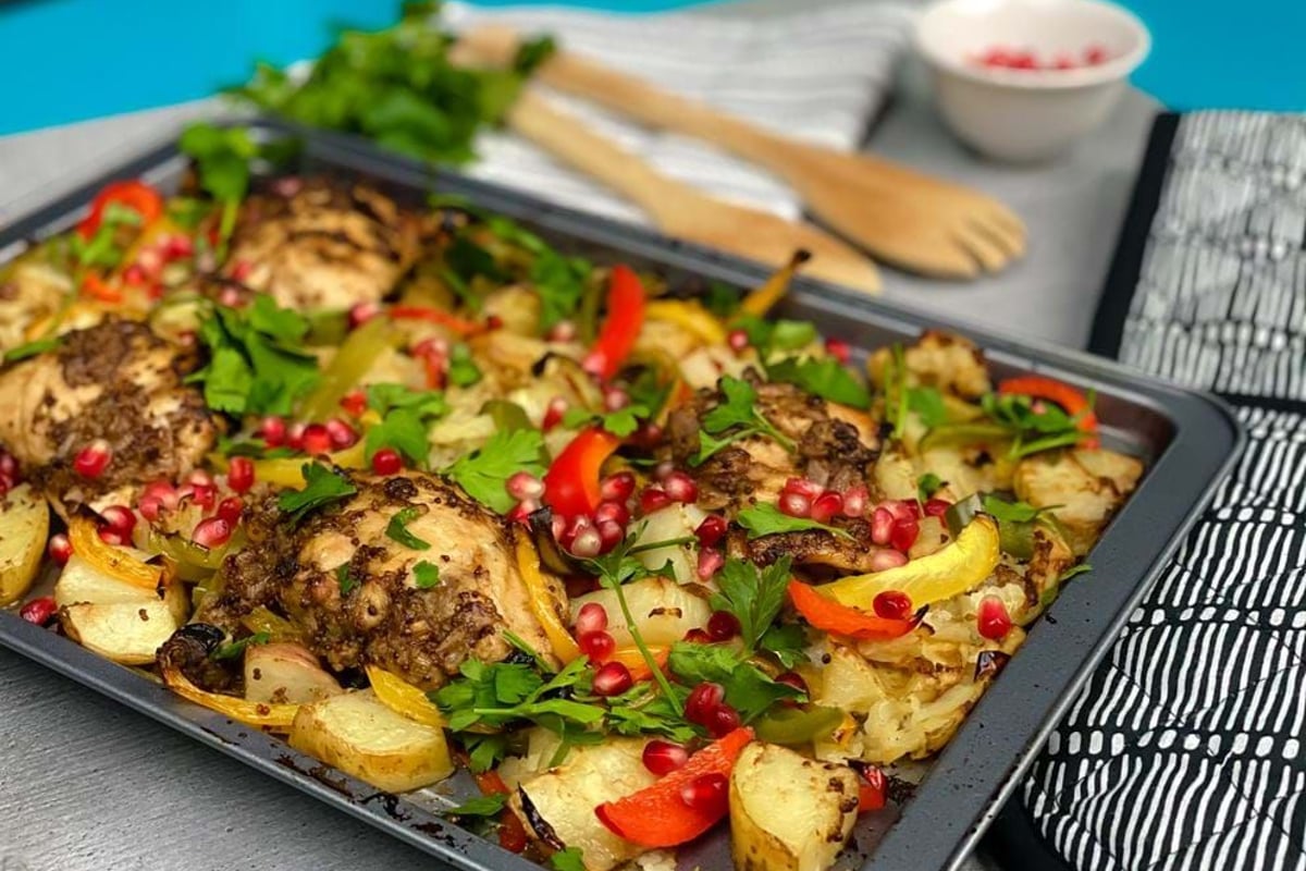 Tray of roasted chicken thighs with potatoes, peppers, parsley, and pomegranate seeds