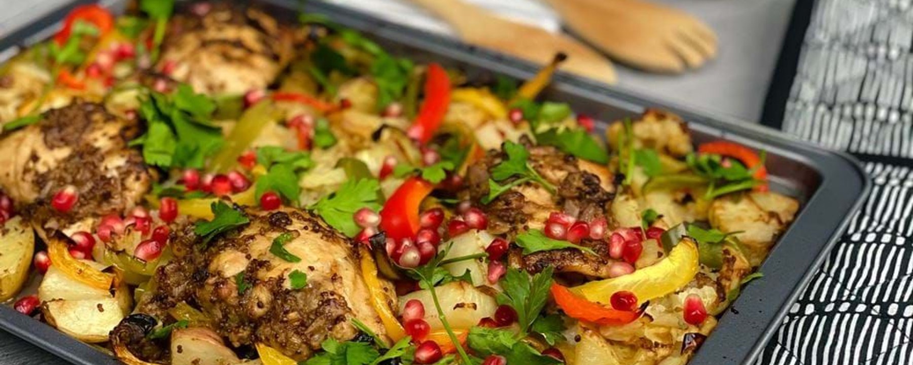Tray of roasted chicken thighs with potatoes, peppers, parsley, and pomegranate seeds