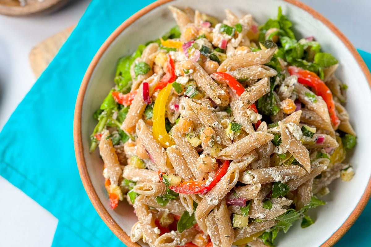 Wholegrain pasta salad with chickpeas, peppers, feta and leafy greens in a white bowl