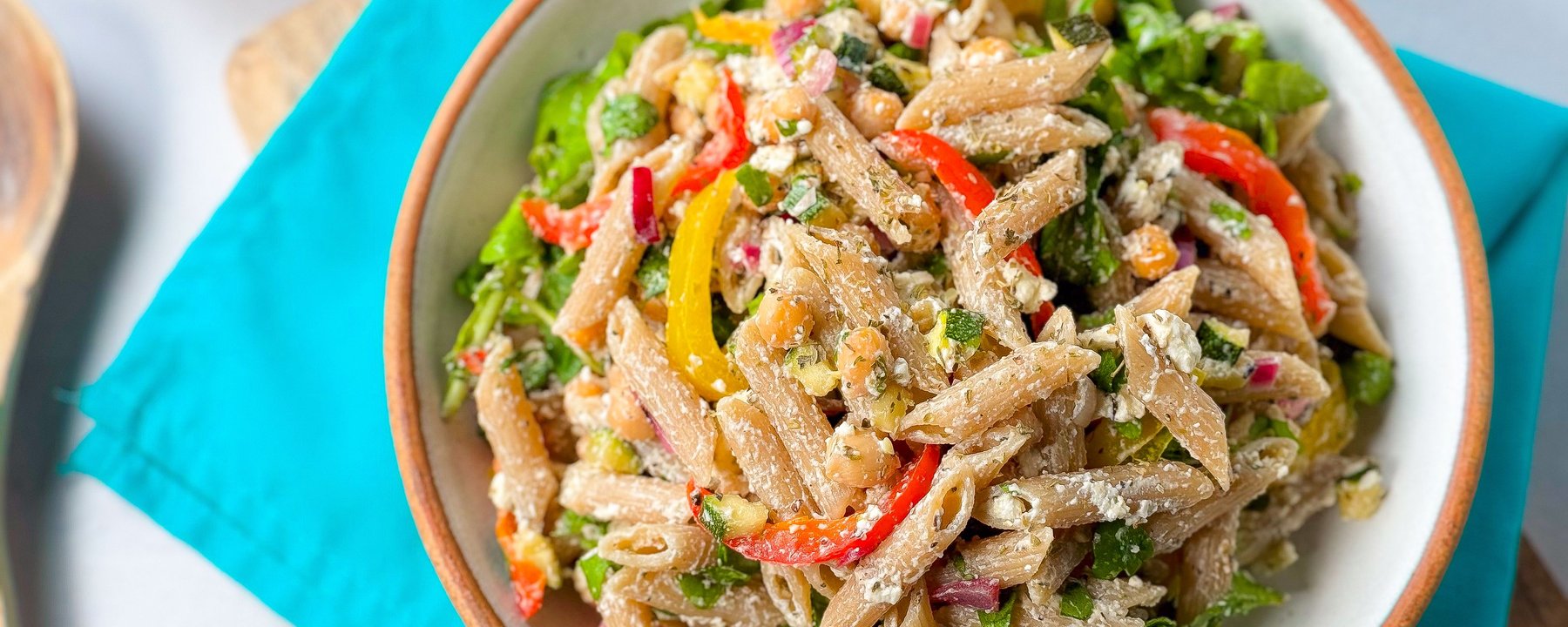 Wholegrain pasta salad with chickpeas, peppers, feta and leafy greens in a white bowl