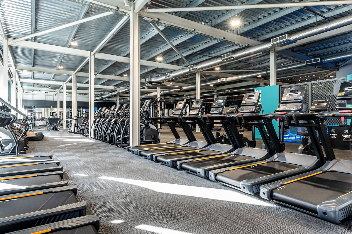 PureGym Bristol Union Gate: Rows of treadmills in a well-lit gymnasium with open ceiling structure and supporting pillars.