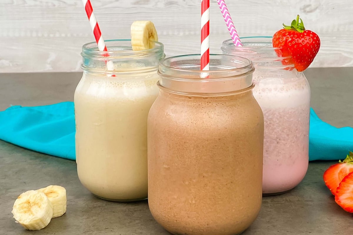 Three jars of milkshakes with striped straws, banana slices, and a strawberry garnish.