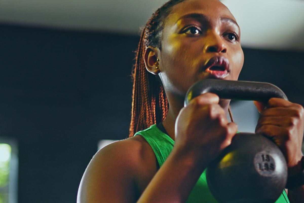 Frau im grünen Sporttop hält Kettlebell mit konzentriertem Gesichtsausdruck beim Training