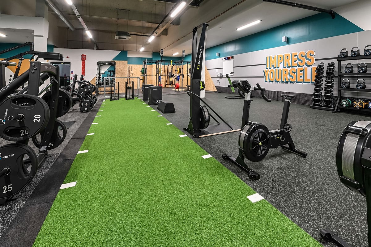 PureGym London Bethnal Green: Weightlifting area with squat racks, free weights, green turf, and motivational signage.