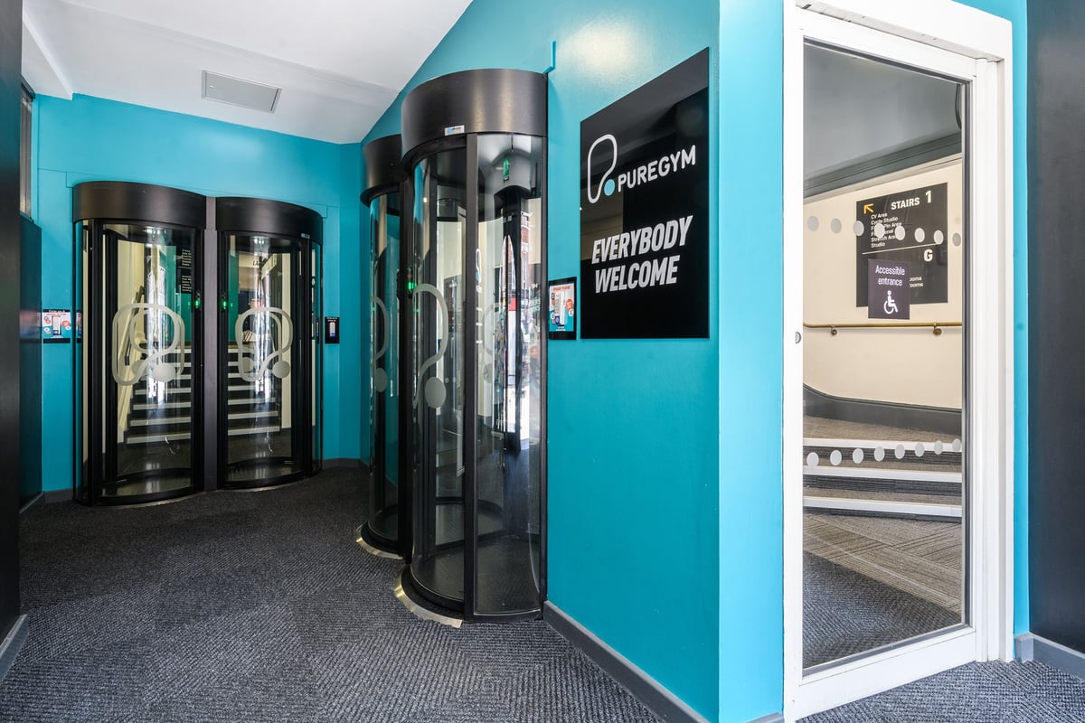 PureGym London Wandsworth: Rows of entrance pods, teal walls, sign stating "Everybody welcome."