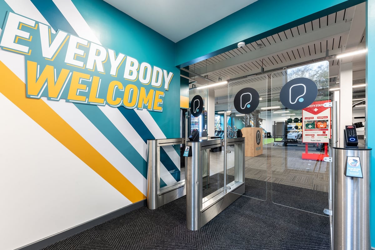 PureGym Glasgow Milngavie: Turnstiles, welcome signage, and self-service kiosks at gym entrance.