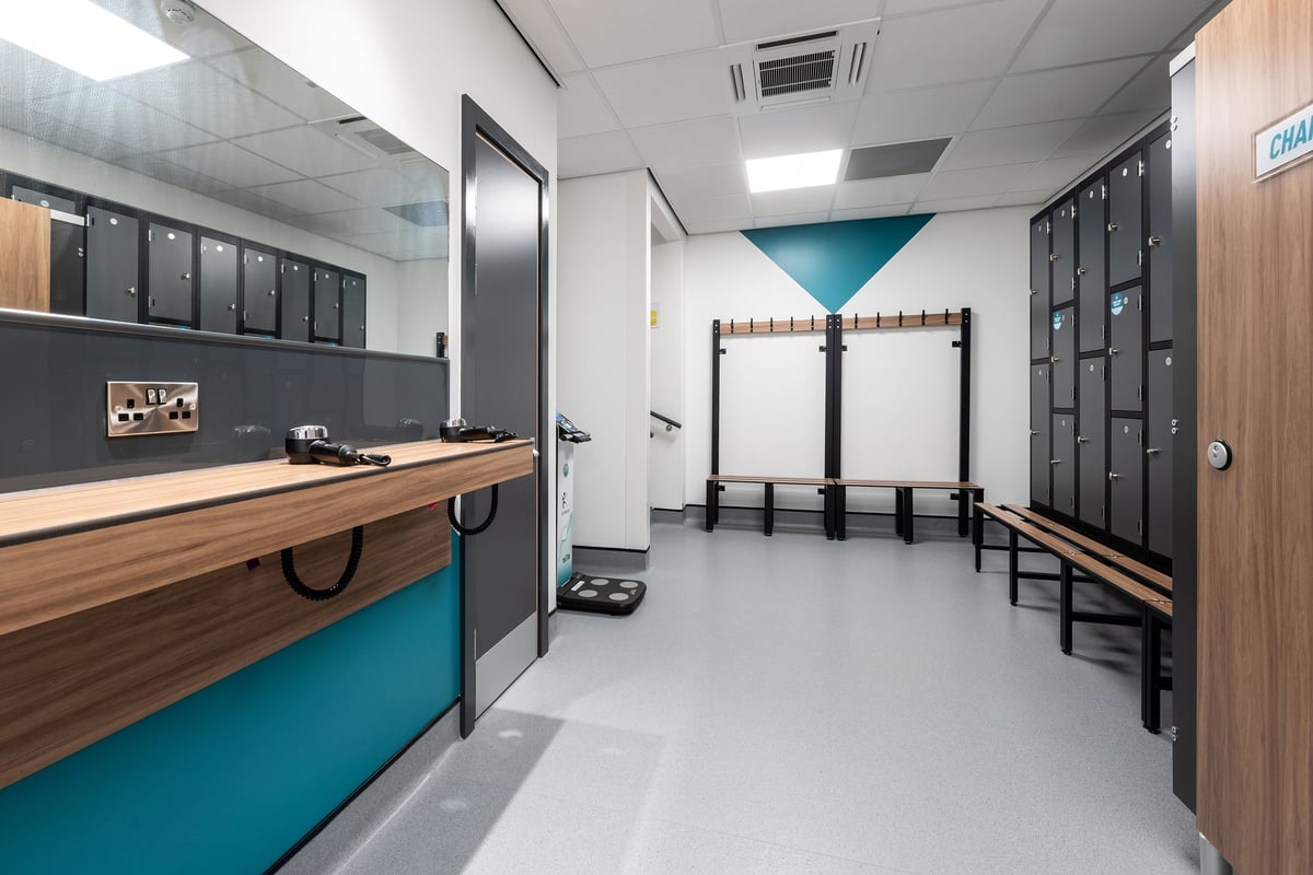 PureGym Bridgend: Locker room with benches, cubbies, coat hooks, and wood-accented counter.