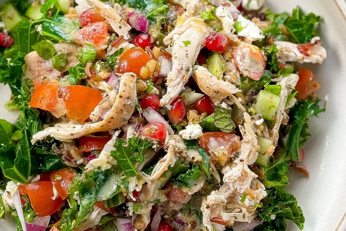 Salad with shredded chicken, kale, tomatoes, pomegranate seeds, cucumber, and onions in a