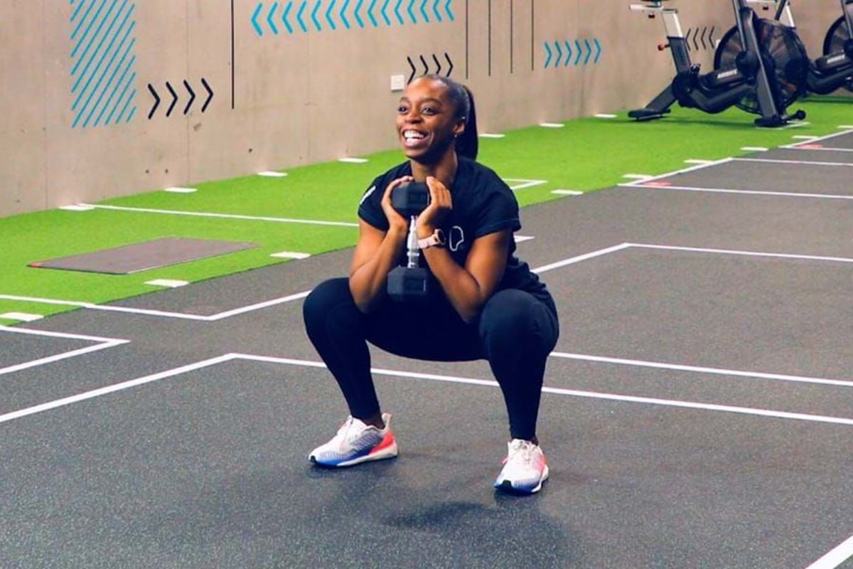 Woman in sportswear doing a goblet squat with a dumbbell in a gym area