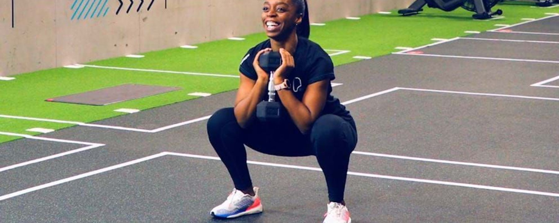 Woman in sportswear doing a goblet squat with a dumbbell in a gym area