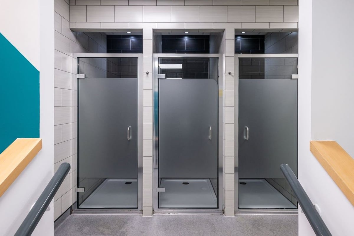 PureGym Wrexham: Grey changing cubicles, tiled walls, and benches in a gym