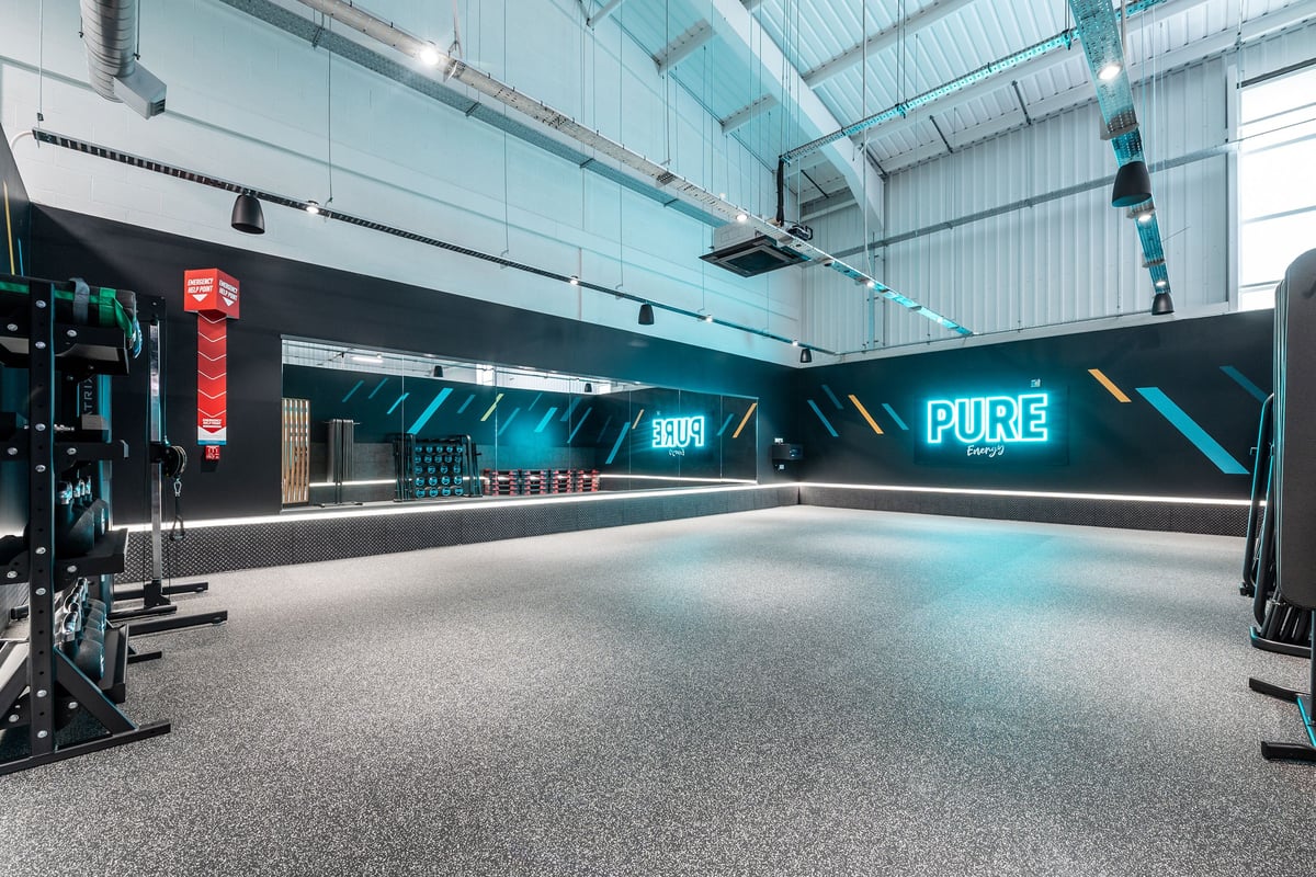 PureGym Winchester: Teal and black studio space with neon signage, rubberized flooring, and workout equipment.
