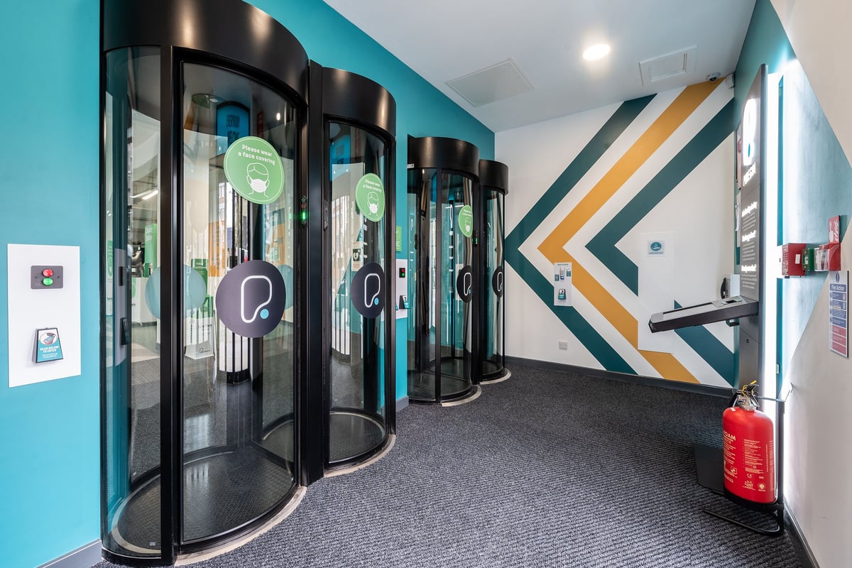 PureGym London Holloway Road: Rows of futuristic-looking entry gates with mirrored panels in a teal and black gym studio.