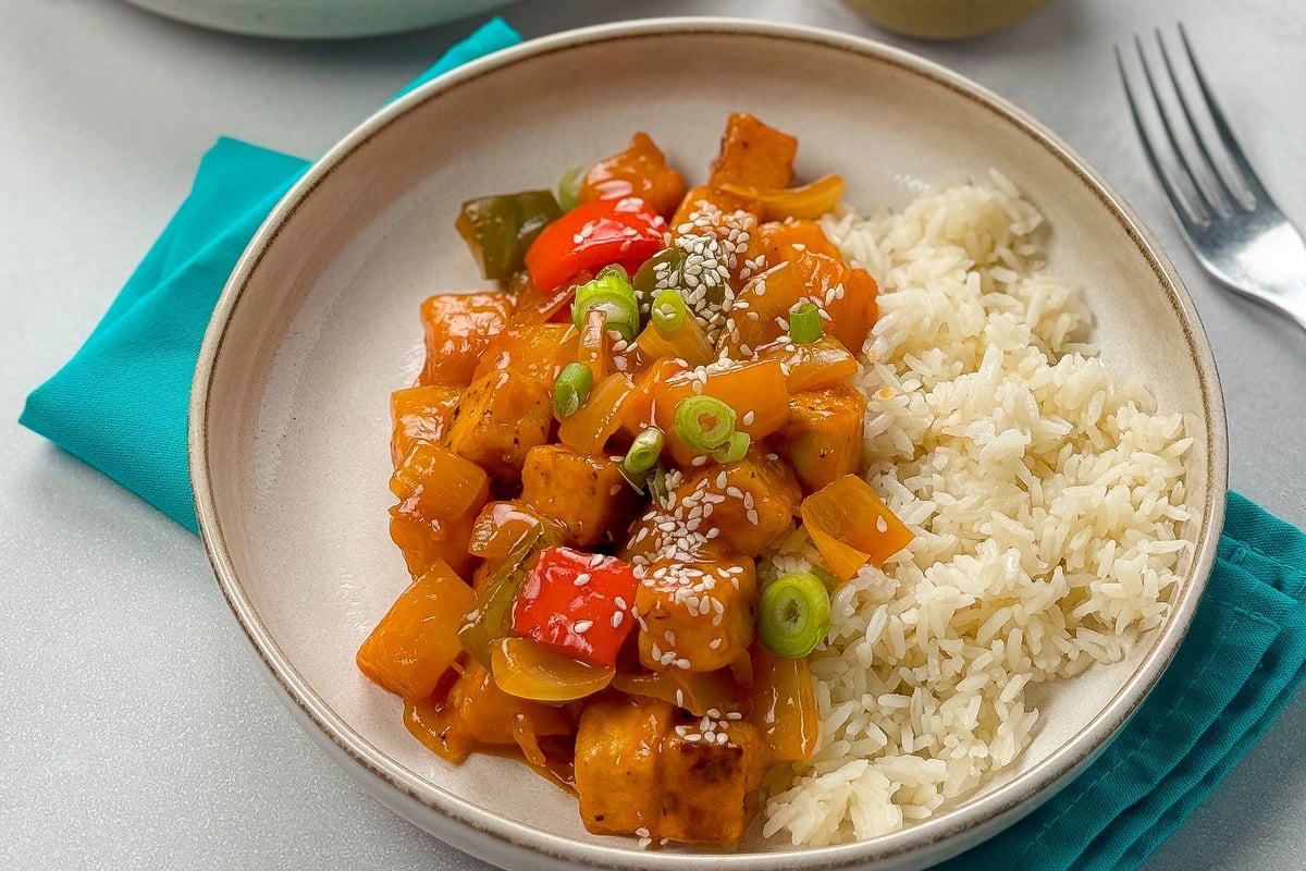 Tofu pieces with peppers in sweet and sour sauce served with white rice in a bowl