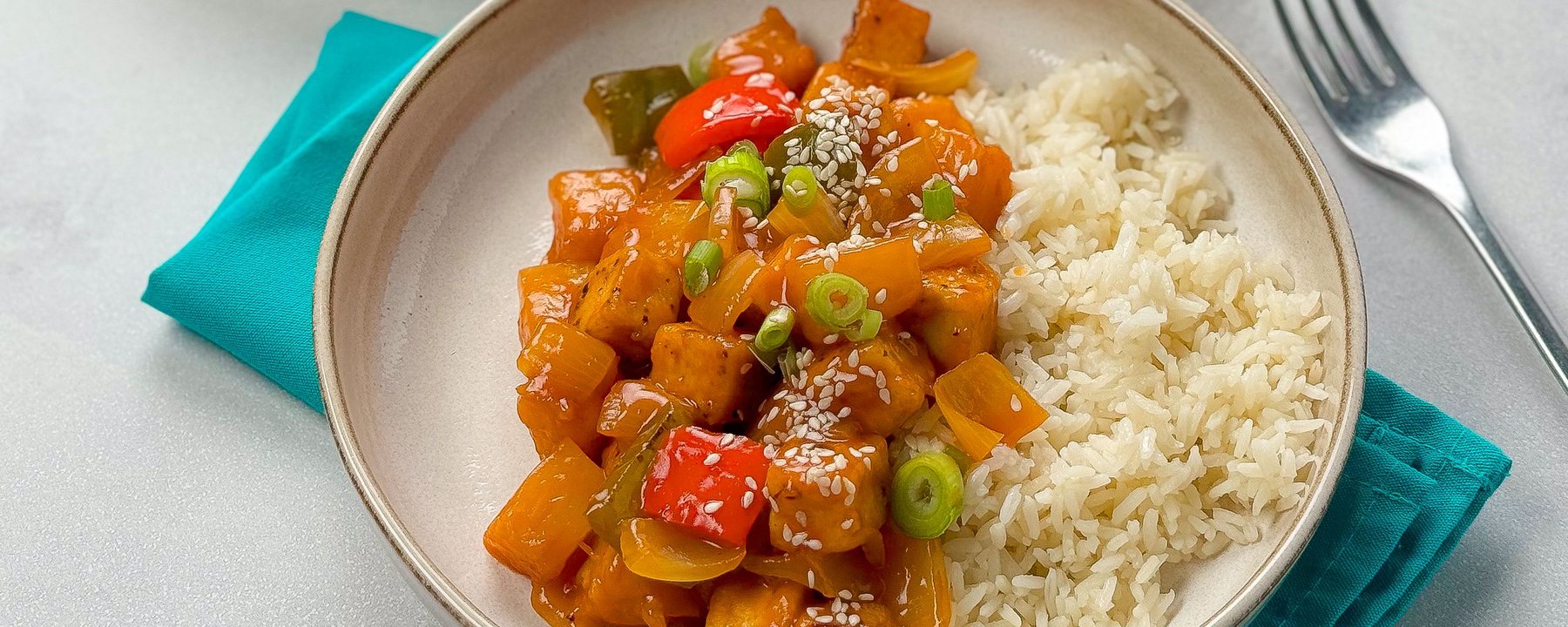Tofu pieces with peppers in sweet and sour sauce served with white rice in a bowl