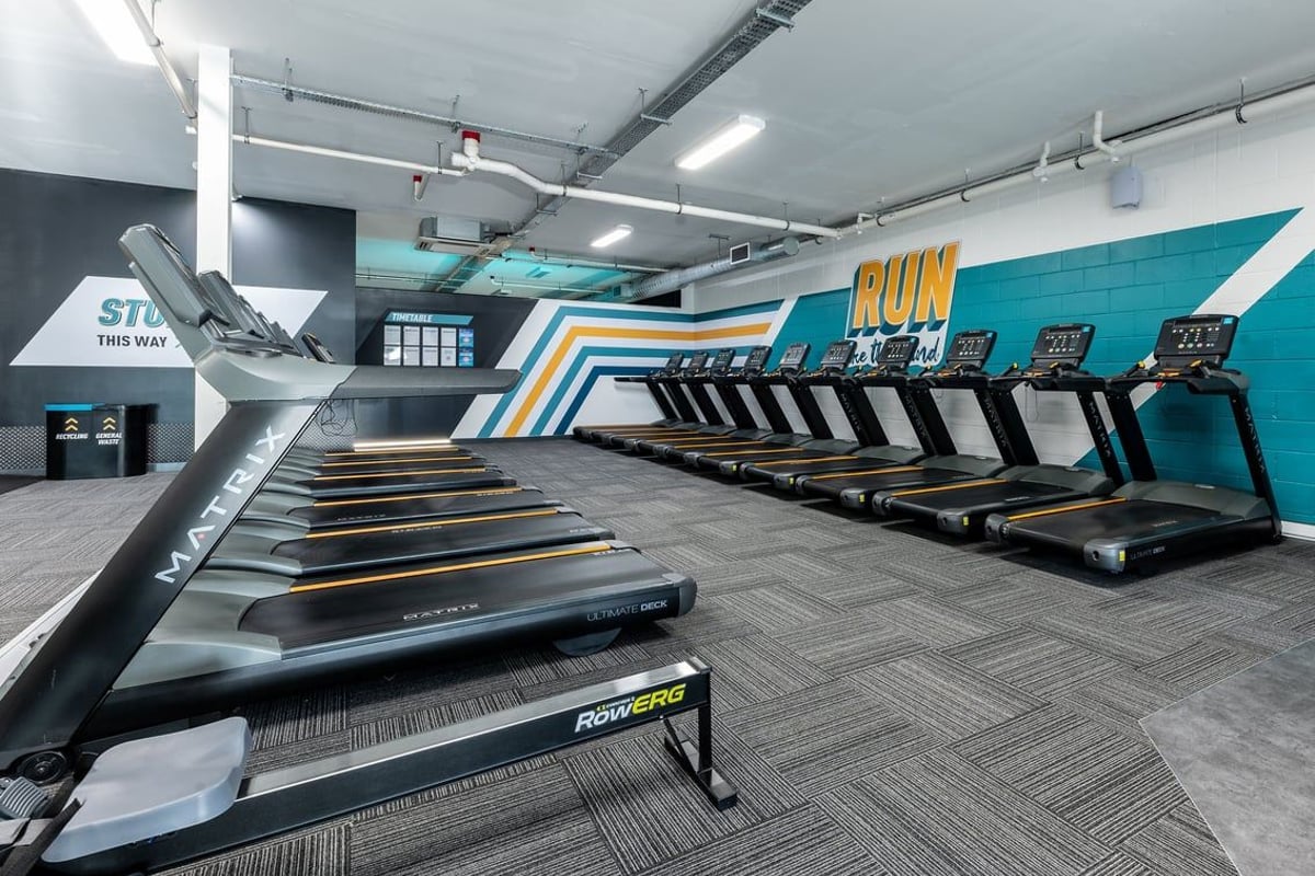 PureGym Ashton Under Lyne: Rows of treadmills, sleek grey flooring, teal accent wall with 'RUN' signage.