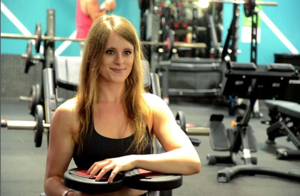 Woman in black sportswear holding weight plates in gym with exercise equipment behind her