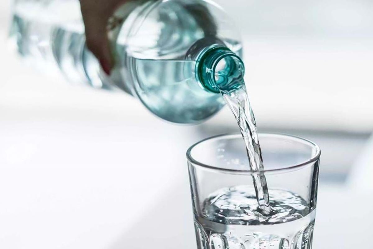 Clear water being poured from a plastic bottle into a glass on a white surface