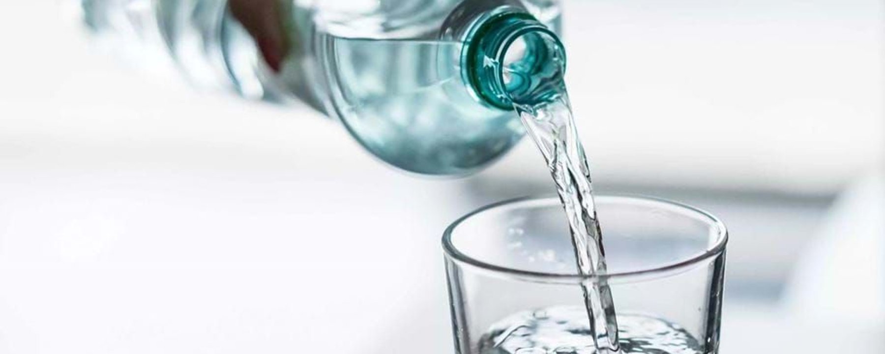 Clear water being poured from a plastic bottle into a glass on a white surface