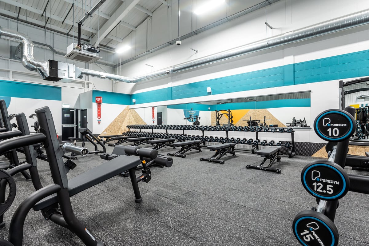 PureGym Winchester: Rows of weight benches, free weights, and mirrored walls in a bright fitness centre interior.