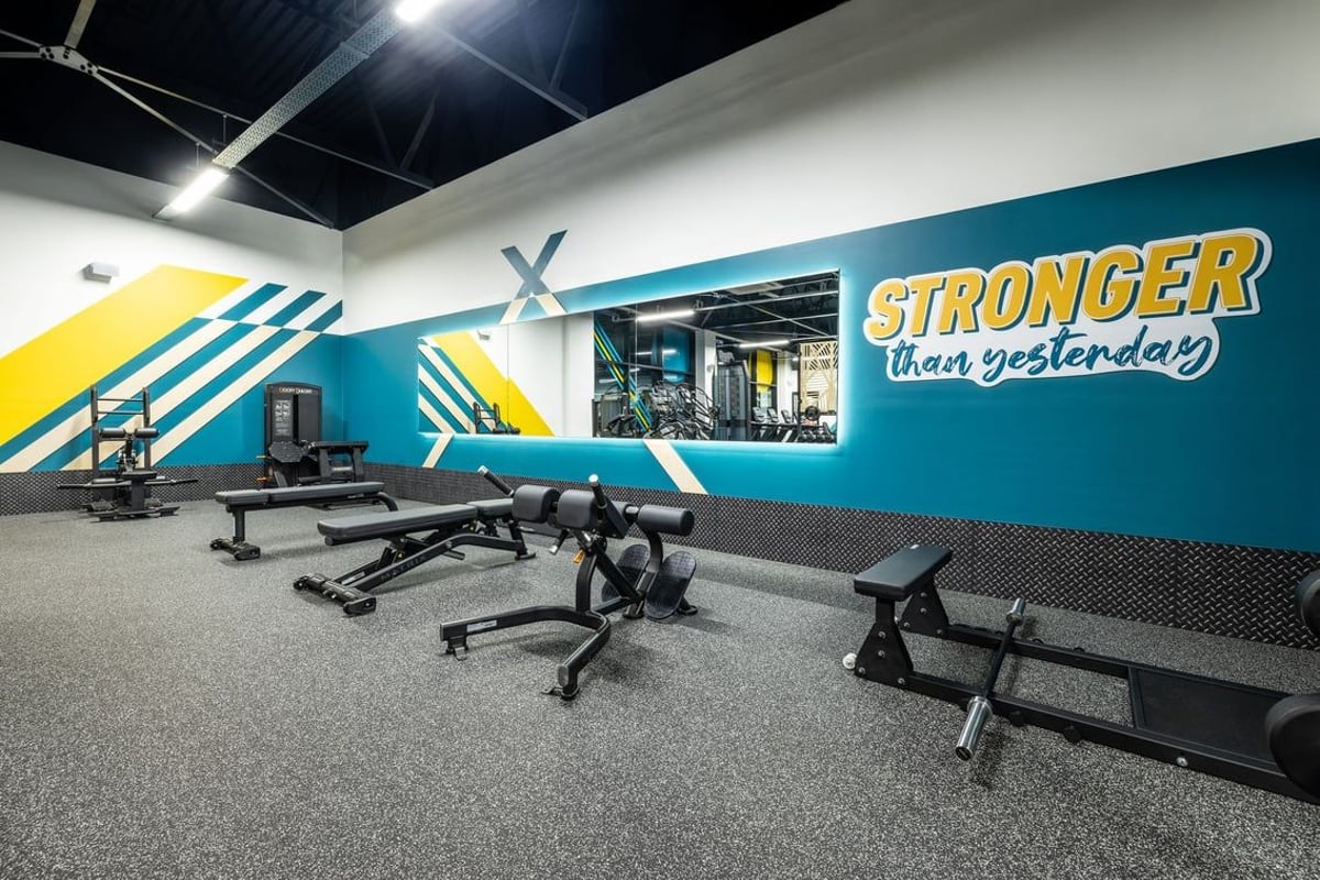 PureGym Washington: Weight benches, free weights, rubberized flooring inside gym with motivational wall graphics.