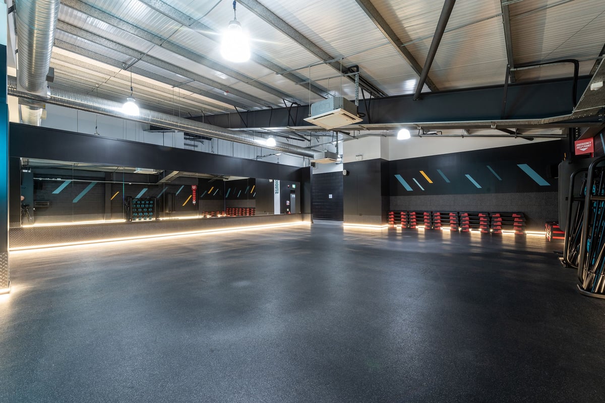 PureGym Banbury Cross Retail Park: Empty gym studio, rubberised flooring, neon lighting, exposed ceiling beams.