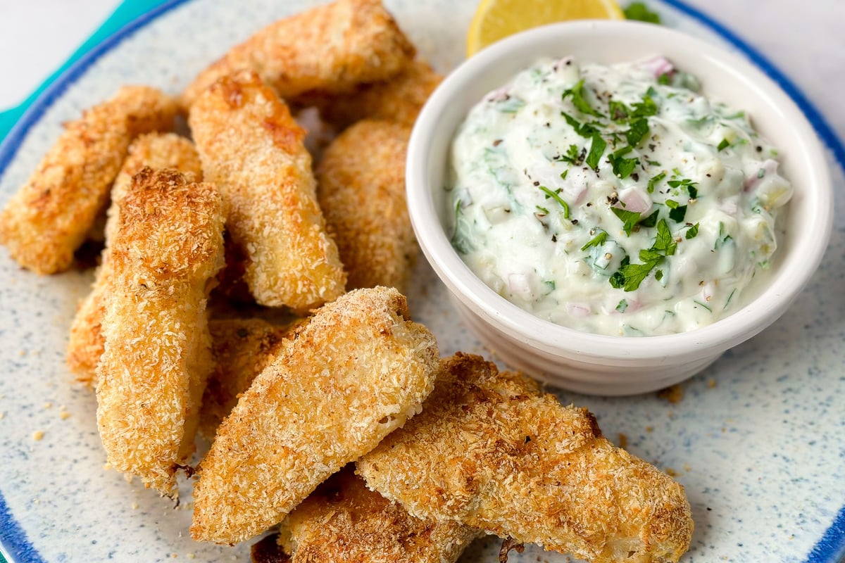 Breaded fish goujons on a plate with creamy tartare sauce garnished with herbs