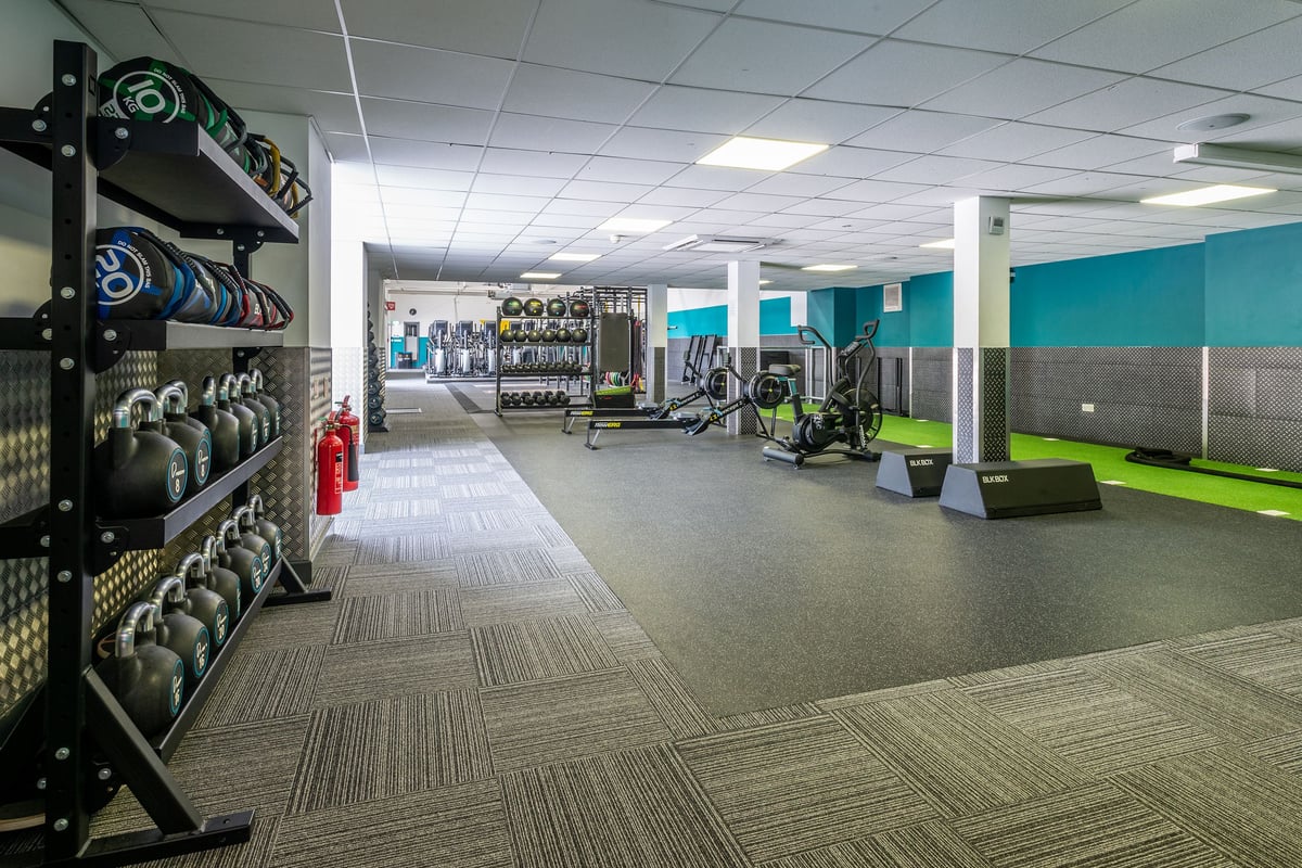PureGym Northwich: Rows of dumbbell racks, weight plates, resistance machines, and rubberized flooring in a gym setting.