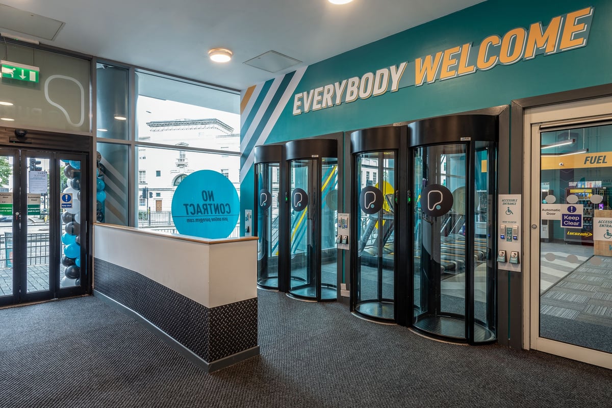 PureGym Leicester St Georges Way: Revolving glass doors, welcome signage, and an exercise studio beyond.