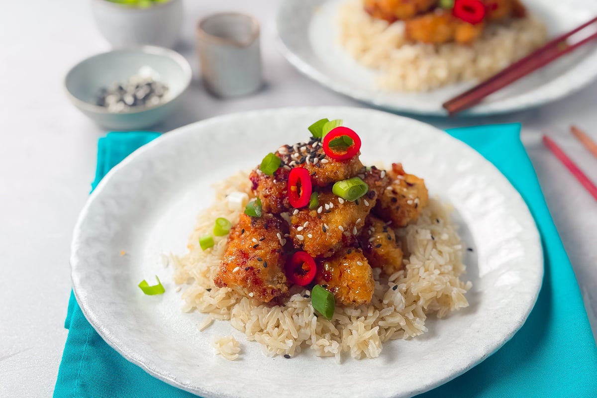 Crispy chicken pieces on rice garnished with red chili slices, spring onions, and sesame