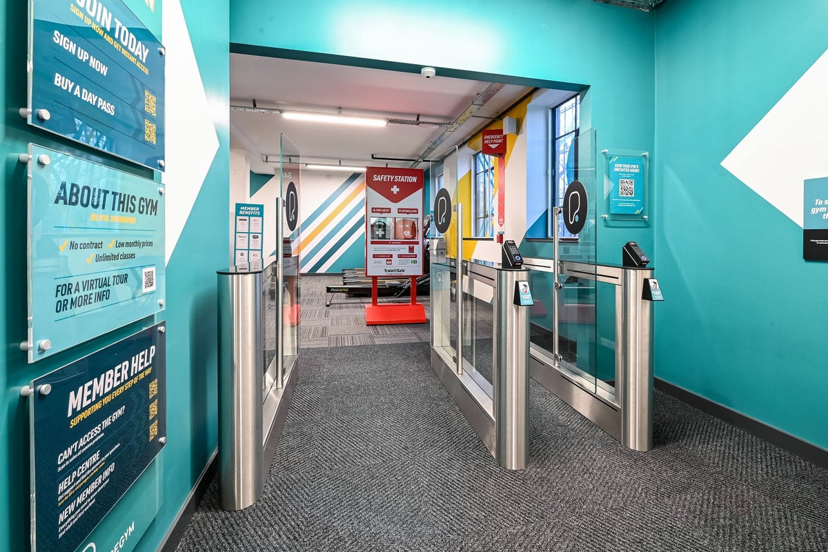 PureGym London Bethnal Green: Turnstiles, signs about memberships, and a corridor leading into a gym facility.