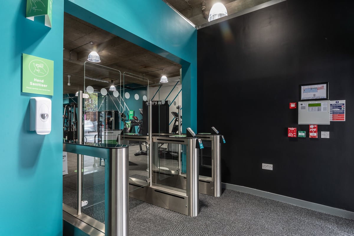 PureGym London Leytonstone: Turnstiles, sanitizer dispenser, and signage at entrance of fitness centre.