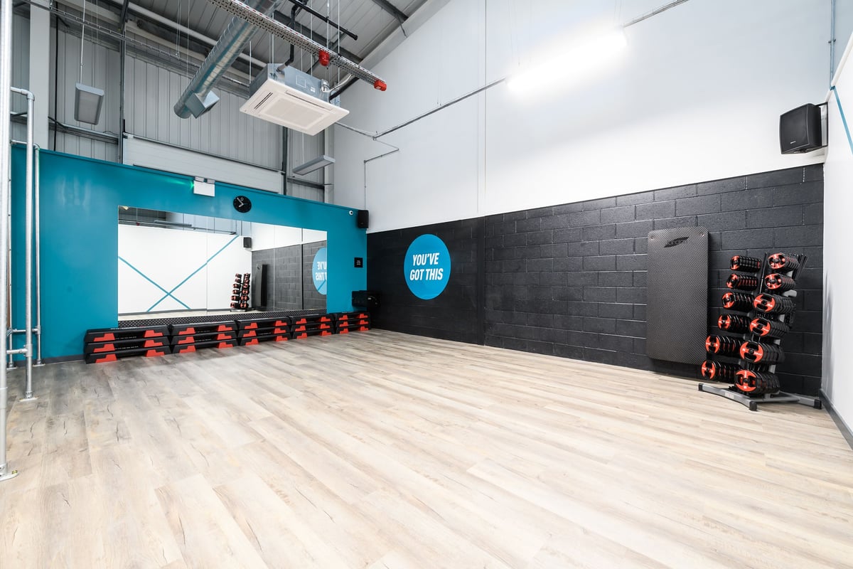 PureGym Buckingham: Teal and grey studio with weight racks, rubberized floors, mirrors, and motivational signage.