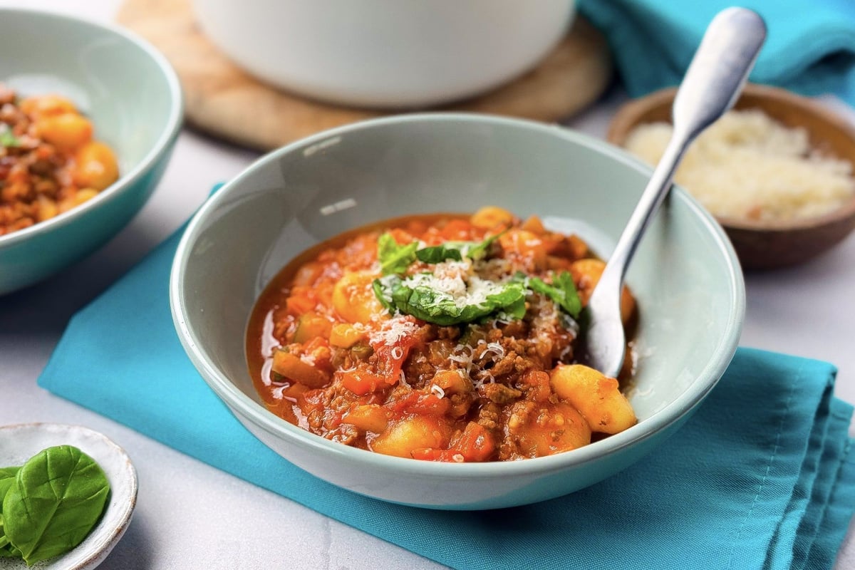 Bowl of gnocchi in tomato sauce with grated cheese and basil on a blue napkin