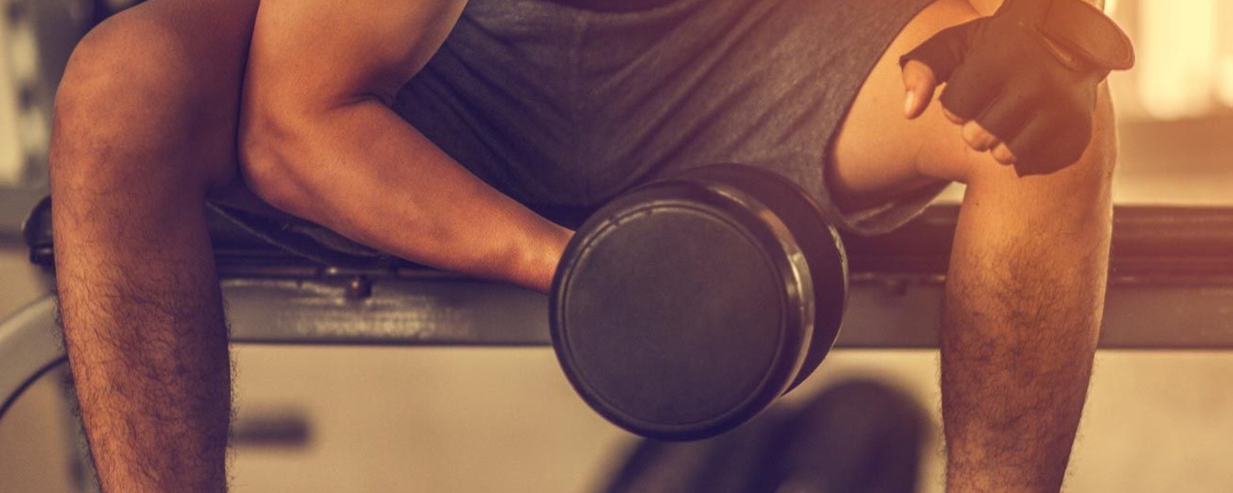 Homme soulevant un haltère assis sur un banc de gym, portant gants et short