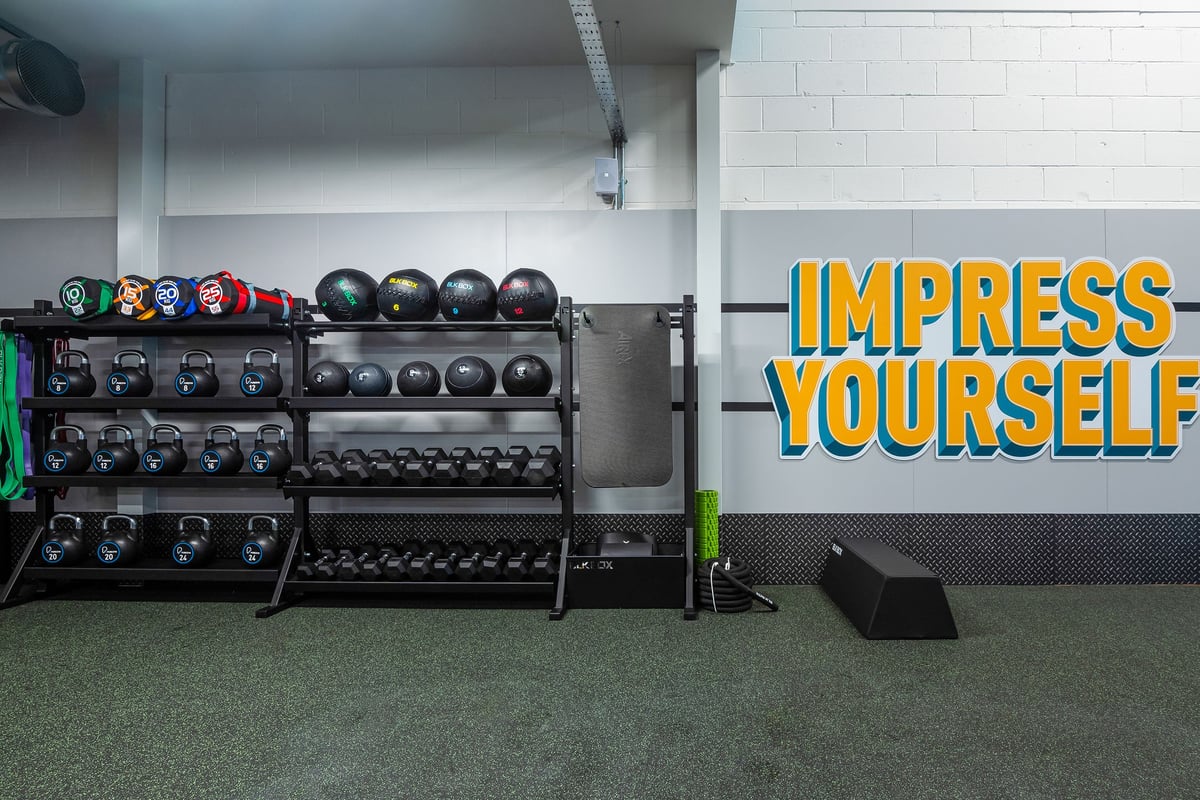 PureGym Linlithgow: Racks of weight plates, barbells, and motivational wall signage in a gym setting.