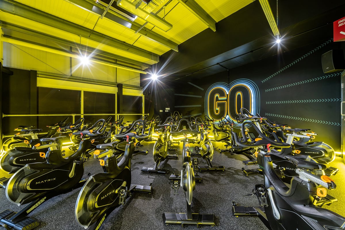 PureGym Wirral Bidston Moss: Rows of stationary exercise bikes in a brightly lit yellow-tinted gym studio.