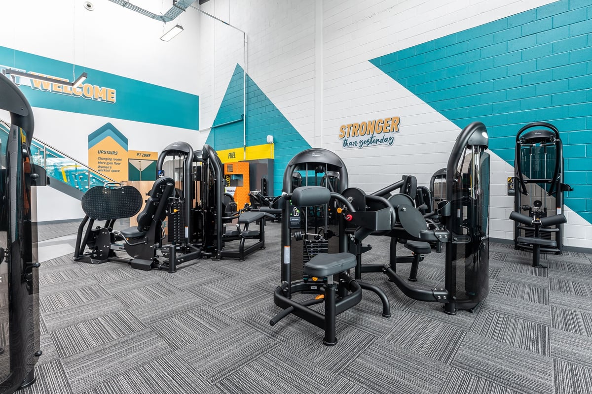PureGym Dewsbury: Rows of black strength training machines, free weights, benches on patterned rubber flooring.