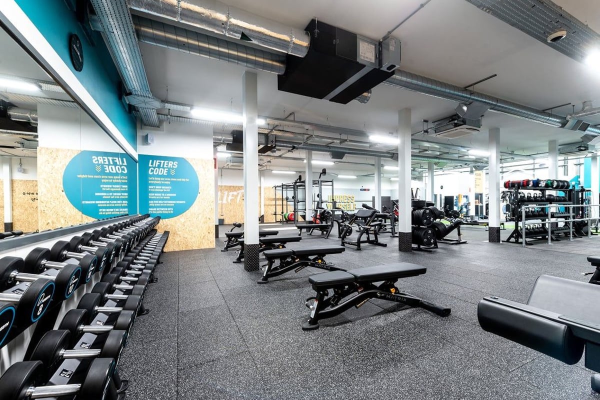 PureGym Ormskirk: Rows of weight benches, free weights, and strength equipment in a modern gym with teal accents.