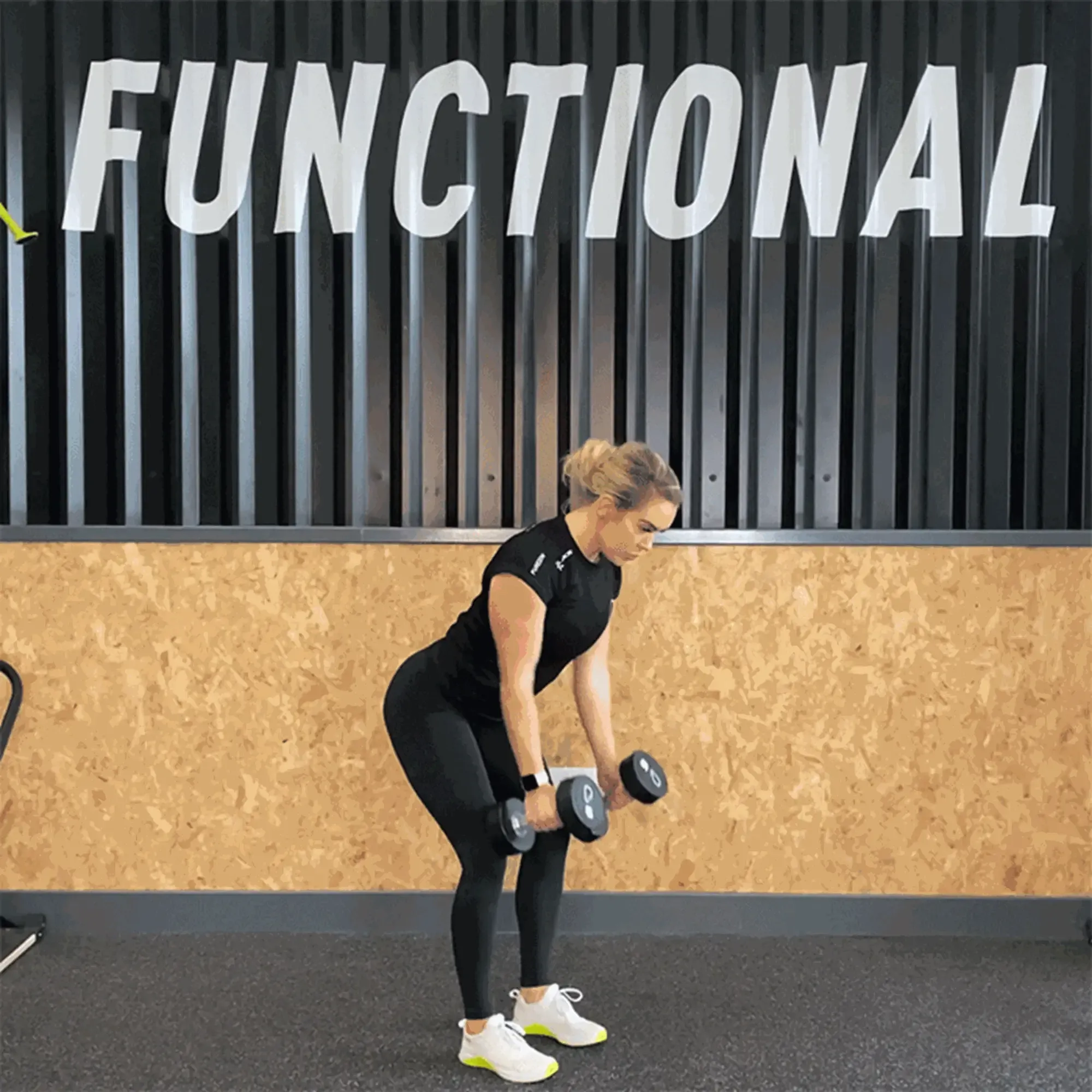 Woman in black workout clothes lifting dumbbells in gym with functional sign above